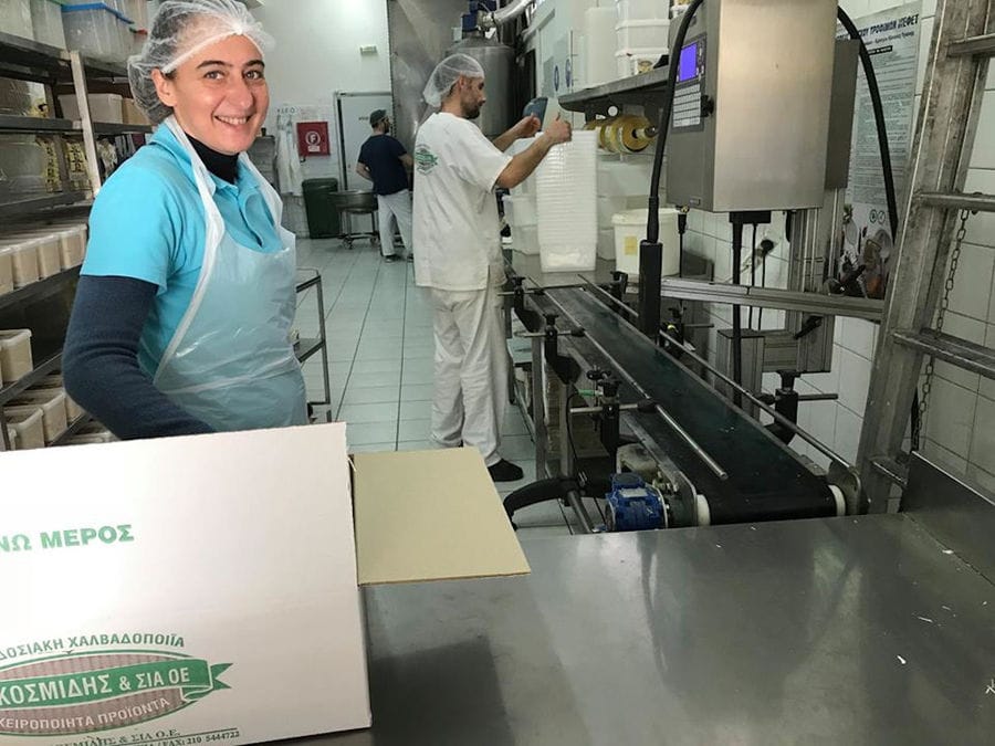 woman smiling at the camera and a man working to labeling machine at 'M. Kosmidis' workshop